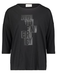 Schwarzes T-Shirt aus weichem Material mit einem großen, glänzenden, schwarzen Textdesign, das "GOOD ENERGY" in unterschiedlichen Schriftarten und -größen zeigt.
