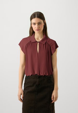 Bordeaux plisserte bluse med krage og nøkkelhulldetalj, med cap sleeves og rynket kant, kombinert med en mørk denimskjørt.