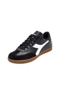 Sneaker nera con tomaia in suede e pelle, strisce bianche a contrasto, lacci piatti e suola in gomma color caramello; design aerodinamico e a profilo basso.