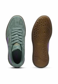 Baskets en daim vert avec un accent violet, lacets ronds, semelle en gomme texturée dotée de motifs circulaires et un logo subtil sur le côté.