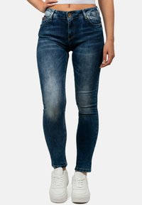 Jeans skinny blu scuro con aree sbiadite, cinque tasche e chiusura con bottone, abbinati a sneaker bianche. Tessuto denim, vita regolare.