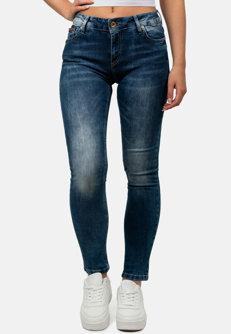 Jeans skinny blu scuro con aree sbiadite, cinque tasche e chiusura con bottone, abbinati a sneaker bianche. Tessuto denim, vita regolare.