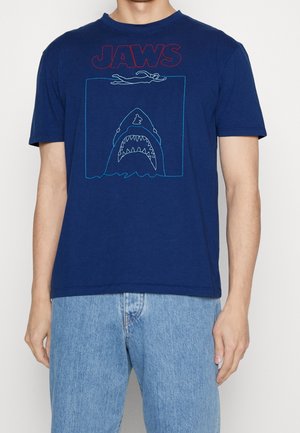 Navyblaue Baumwoll-T-Shirt mit "JAWS" in Rot, versehen mit einer Grafik eines Schwimmers über einem Haifisch, umrandet in Blau. Kurze Ärmel, lockere Passform.