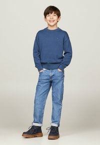 Maglione blu a maglia, jeans in denim azzurri chiari e stivali navy con suole marroni. Il maglione ha un collo rotondo e polsini a coste.