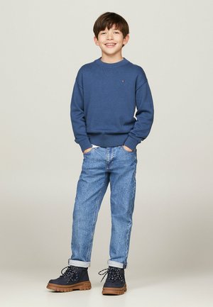 Maglione blu a maglia, jeans in denim azzurri chiari e stivali navy con suole marroni. Il maglione ha un collo rotondo e polsini a coste.
