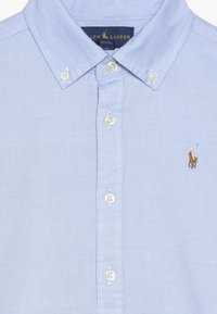 Camicia button-down blu chiaro in cotone, con colletto aperto, bottoni bianchi e logo ricamato di un giocatore di polo sul petto.