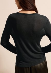 Schwarzes langärmliges Oberteil mit rundem Halsausschnitt, weicher Textur und lässiger Passform, von hinten betrachtet, kombiniert mit einem dunklen, glänzenden Rock.