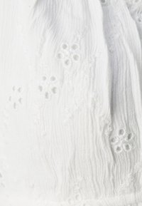 Bílé látky s vyšívanými květinovými očkovými vzory a jemnou vertikální žebrovanou texturou.