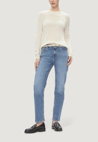 Maglione a maniche lunghe color crema chiaro, jeans dritti blu chiaro e mocassini neri. Maglione con lavorazione a maglia texturizzata e discreto dettaglio con logo.