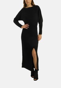 Schwarzes geripptes Strickkleid mit langen Ärmeln und einem seitlichen Schlitz, das eine taillierte Taille und eine gerade Silhouette aufweist. Akzentuiert durch eine glatte Textur.