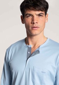 Lichtblauw lange mouwen henley-shirt met een gemarmerde knoopsluiting en zak. Zacht materiaal, ontspannen pasvorm en ronde halslijn.