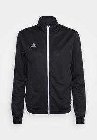 Mustavartinen urheiluvaatteiden takki, jossa on sileä kangas, korkea kaulus ja valkoinen vetoketju, sekä brodeerattu valkoinen Adidas-logo.