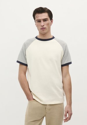 Crème T-shirt met korte mouwen, grijze raglanmouwen en een marineblauwe ribkraag. Zachte textuur, casual pasvorm en contrasterende accenten op de mouwen.