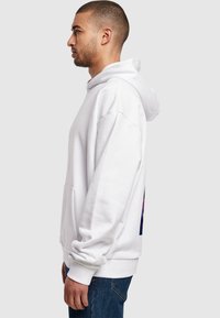 Sudadera blanca con un corte relajado, bolsillo frontal y un gran detalle gráfico colorido en la parte posterior. Textura suave y puños y dobladillo acanalados.
