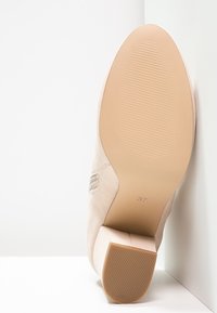 Zapato de tacón alto de ante beige con suela texturizada y acabado mate. Tacón cuadrado y punta redonda, talla 37. Sutiles acentos laterales visibles.