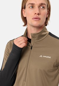 Heren Vaude kwart-rits top in kaki met zwarte mouwen, gemaakt van zachte, rekbare stof; heeft een klein logo en ritsdetails.
