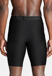 Schwarze Kompressionsshorts aus dehnbarem Material, mit einem breiten Bund, der das "UNDER ARMOUR"-Logo trägt, und einer glatten Textur.