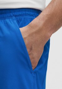 Blaue Sportshorts mit elastischem Bund und seitlicher Tasche, aus leichtem, glattem Stoff mit subtiler Textur.
