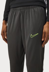 Grijze sportbroek gemaakt van lichtgewicht materiaal, met een elastische tailleband en een neon groene Nike-logo op de linker bovenbeen.