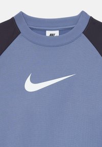 Plavi i crni Nike dukserica s rebrastim okruglim izrezom i bijelim Nike swoosh logotipom centrira na prsima.