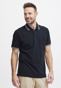 Svart polo skjorte med en brettet krage med blå og hvite striper, kortermet og med brystlomme. Strukturert stoff.