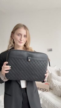 Schwarze, gesteppte Laptophülle mit einer glatten Oberfläche, goldenen Akzenten und einem Reißverschluss. In einem neutralen, modernen Umfeld präsentiert.