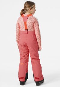 Pantalones de esquí rosa con tirantes ajustables naranjas, tejido texturizado y puños inferiores negros. Vista trasera, con el logo en la pierna izquierda.