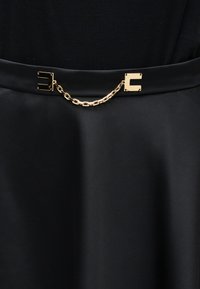 Μαύρη φούστα με ψηλή μέση και χρυσή ζώνη αλυσίδας που διαθέτει δύο ορθογώνιες πόρπες συνδεδεμένες με μια κοντή αλυσίδα.