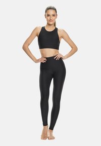 Zwarte sportset bestaande uit een mouwloos cropped topje en high-waist leggings, beide gemaakt van een glad, rekbaar materiaal voor comfort en bewegingsvrijheid.