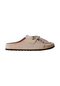 Mocassin beige en daim sans talon avec semelle noire, pompons décoratifs et accents de perles métalliques sur le dessus.