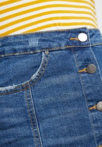 Blå jeanskjol med hög midja, med fransig fickkant och flera metallknappar. Mjuk textur, subtila blekningsdetaljer.