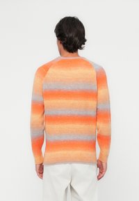 Maglione lavorato a maglia con audaci strisce orizzontali in arancio, pesco e grigio chiaro. Texture a coste, maniche lunghe e scollo rotondo.