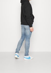 Sudadera negra con capucha, jeans ajustados azul claro y zapatillas blancas con detalles azules. Diseño sencillo, silueta entallada y estilo casual.