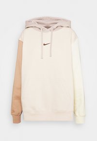 Krämm och beige färgblockerad hoodie med känguruficka, dragsko på huvan och liten brun Nike-logotyp på bröstet. Mjuk textur.