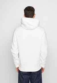 Biała hoodie z kapturem i kieszenią kangurką, z prążkowanymi mankietami i dołem. Miękka tekstura, luźny krój i duży kaptur z tyłu.