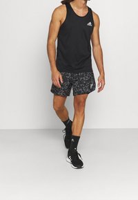 Top sportivo nero con un piccolo logo, abbinato a pantaloni corti leopardati in bianco e grigio. Gli accessori includono calze nere e scarpe da ginnastica.