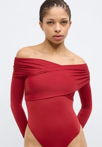 Punane pika varrukaga bodi, millel on õlgadest avatud disain, õlgadel kortsus tekstuur ja ühtlane sile kangas.