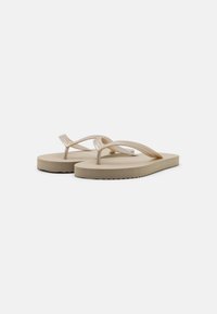 Tan flip-flops featuring a smooth rubber sole, textured fabric straps, a molded footbed, and a zigzag-patterned outsole for grip.