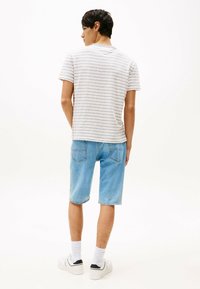 Stribet grå og hvid kortærmet t-shirt parret med lyseblå denimshorts. Modellen har hvide sneakers og ankellange hvide sokker på.