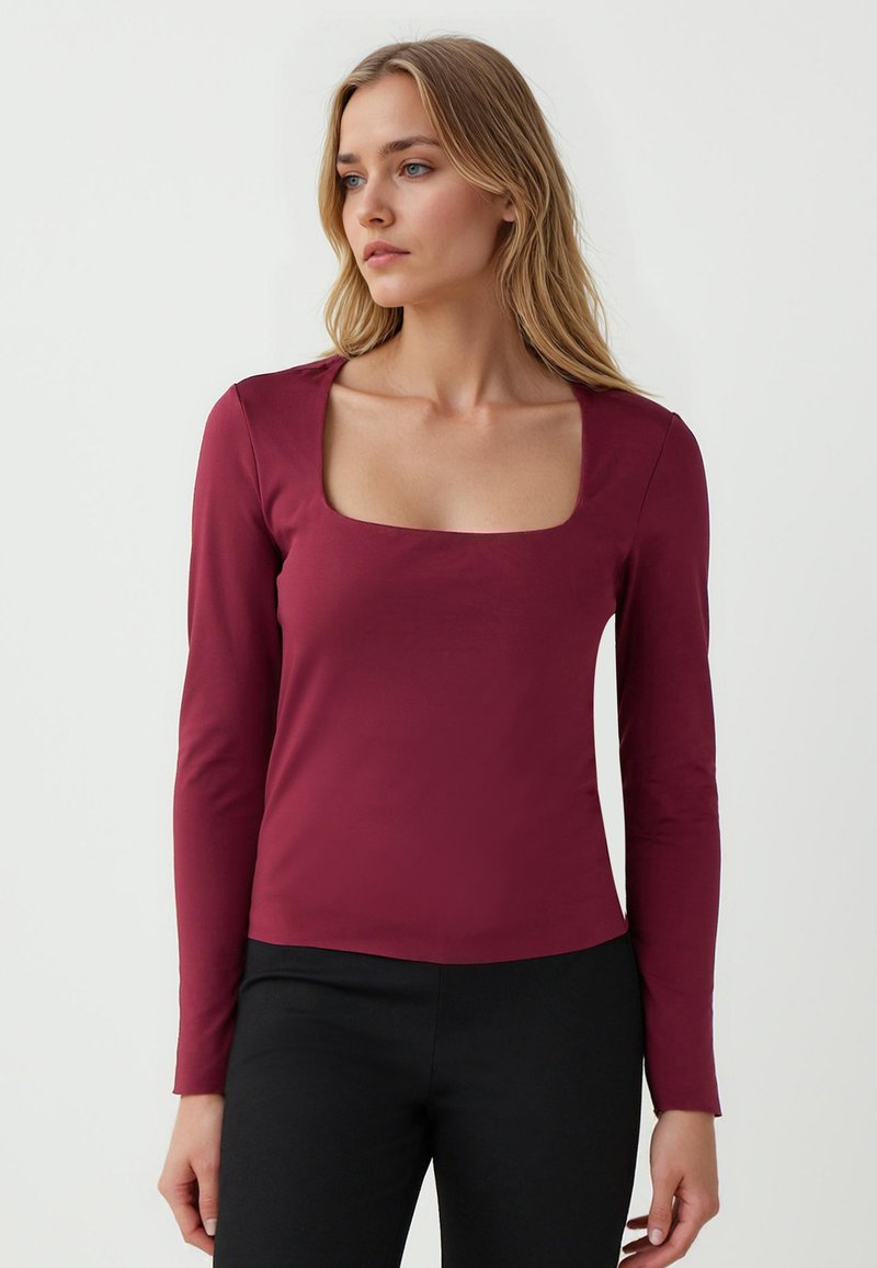 Maglietta a maniche lunghe color bordeaux con scollatura quadrata, realizzata in tessuto morbido, design aderente e stile minimalista, abbinata a pantaloni neri.