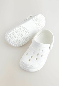 Weiße Clogs mit einem durchlöcherten Design für Atmungsaktivität, aus glattem Kunststoff gefertigt, mit einem Fersenriemen und einer strukturierten Sohle für besseren Halt.