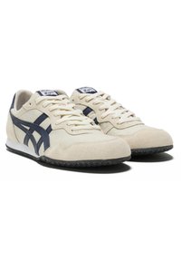 Sneakers in suede beige con dettagli in pelle blu navy, suola in gomma e lacci bianchi. Presentano un design retro e una superficie testurizzata.