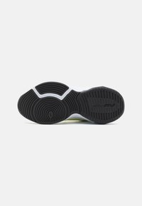 Suela de goma negra con patrones de relieve texturizados y acentos en la entresuela blanca. Presenta un diseño suave y curvado con un detalle amarillo.