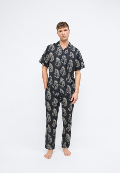 Schwarzes Pyjama-Set mit Muster, bestehend aus einem kurzärmeligen Shirt und langen Hosen, mit beigefarbenen Tiermotiven und einem entspannten Schnitt. Aus Baumwollstoff.