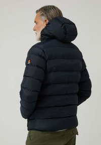 Chaqueta de plumas de color azul marino con capucha, presenta segmentos acolchados horizontales, puños elásticos y un logo en el hombro izquierdo.