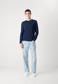 Tengerészeti hosszú ujjú kötött póló; világoskék egyenes lábú farmer; fehér sportcipő. Simább textúra, kerek nyakú, és laza fazon.