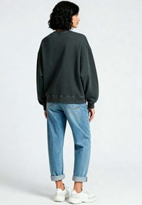 Felpa oversized in carboncino con polsini a costine, abbinata a jeans azzurri risvoltati e sneakers bianche, vista da dietro.