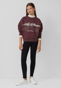 Bordeaux sweatshirt met "NEW YORK" en skyline grafiek, gecombineerd met zwarte leggings en witte sneakers. Beschikt over brede mouwen en een ronde hals.