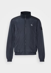 Granatowa nylonowa kurtka z wysokim kołnierzem, zapięciem na zamek z przodu, elastycznymi mankietami i dołem, z dyskretnym logo na piersi oraz teksturowanym wyko�ńczeniem.