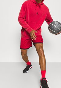 Haut à capuche en polaire rouge avec logo Jordan noir, shorts rouges avec bord noir, baskets noires et un ballon de basket. Mettez l'accent sur le design et les couleurs des vêtements de sport.